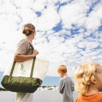 Person holding a tote bag with a scenic background of water and blue sky.