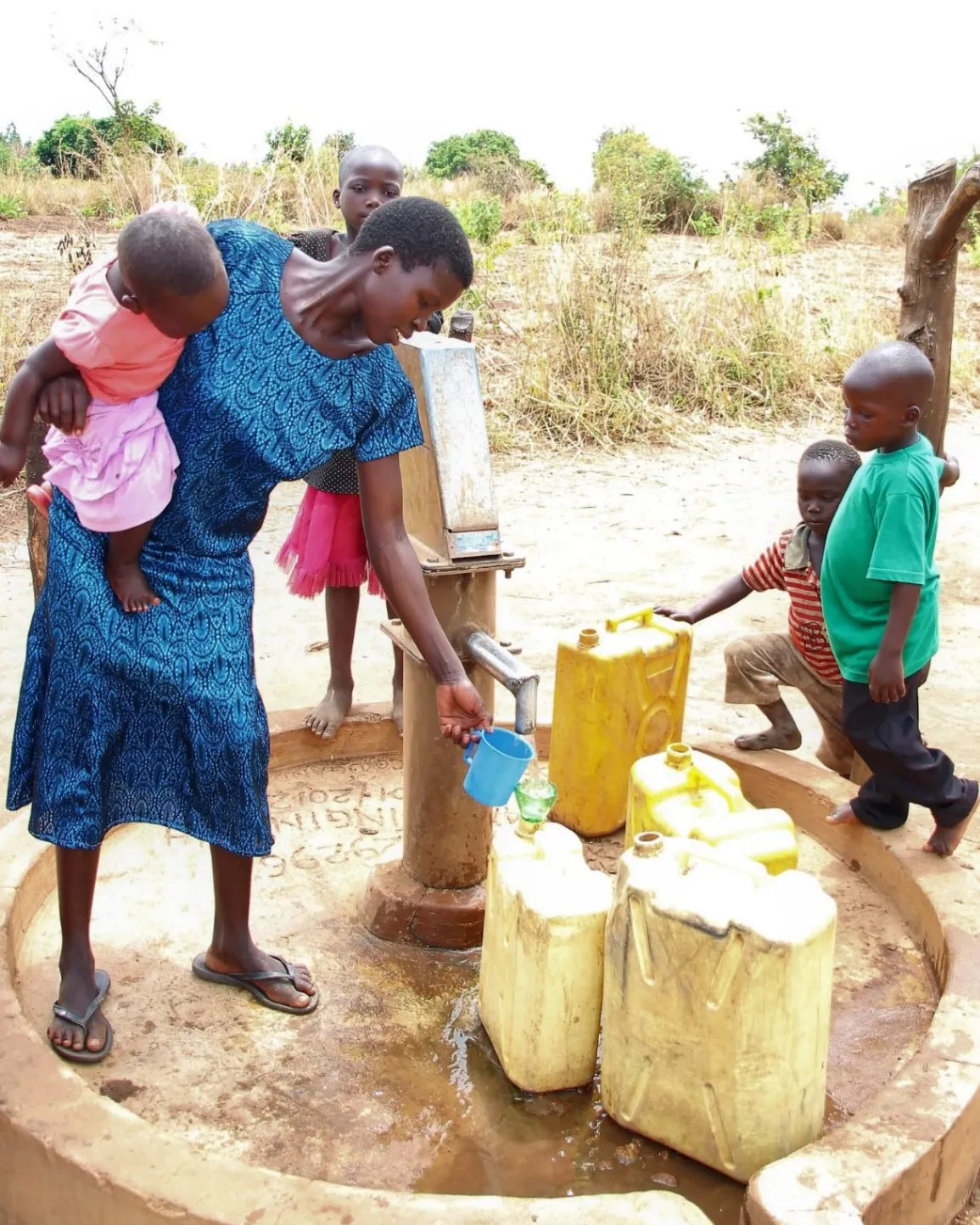 Woman and children at a water well with jerry cans