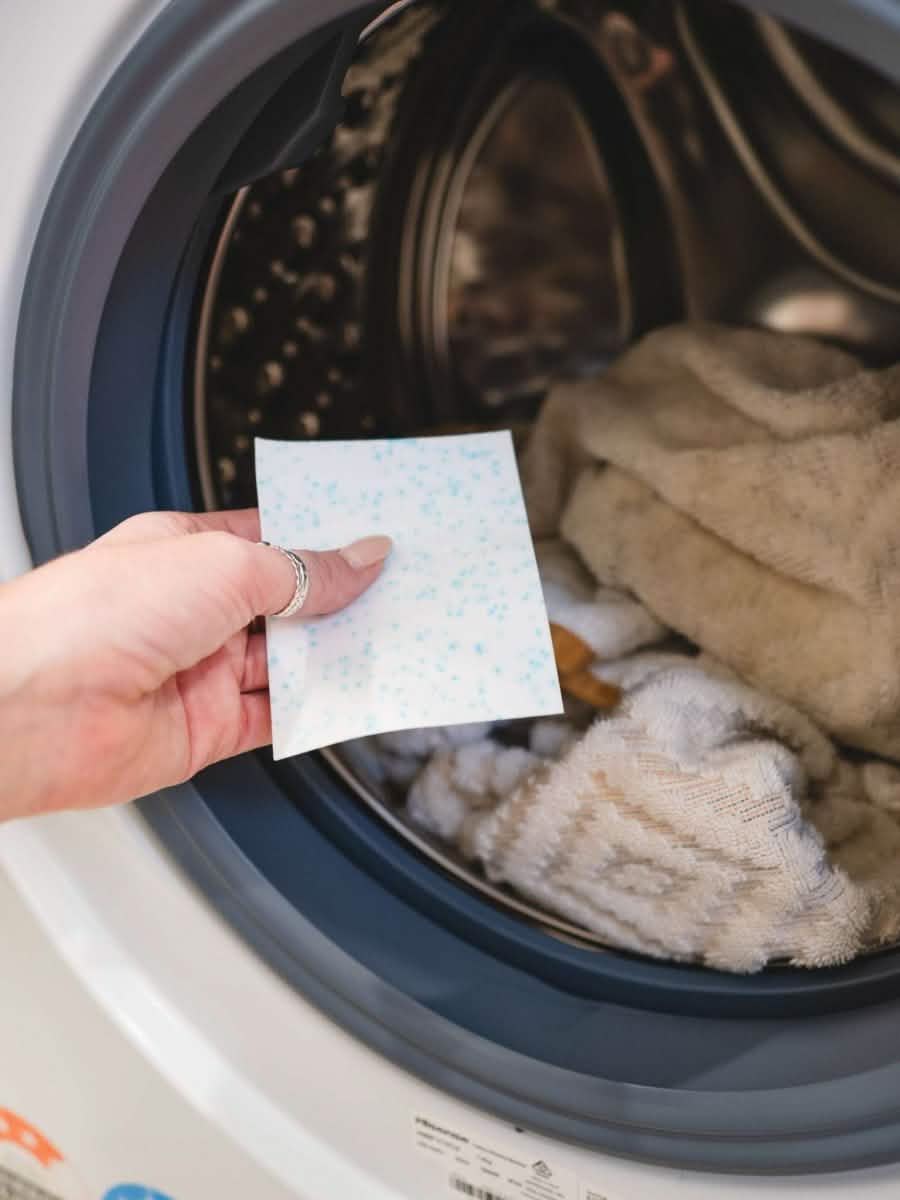 hand putting detergent sheet in machine of towels