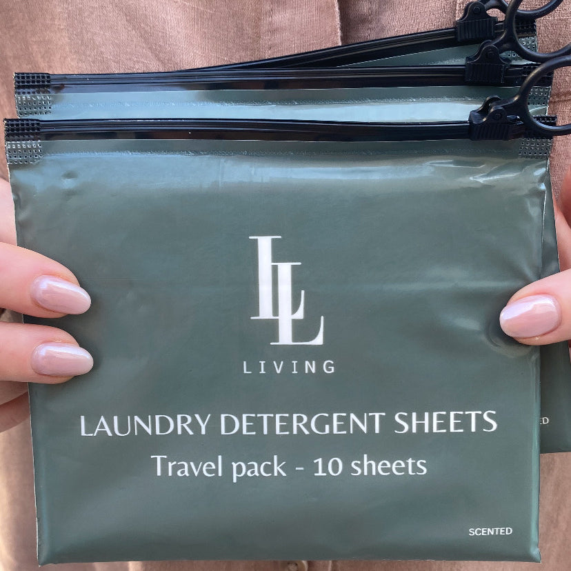 Green travel package of scented laundry detergent sheets held by a person wearing a brown shirt.