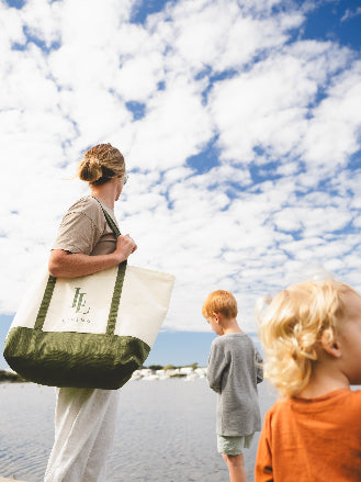 Person holding a tote bag with a scenic background of water and blue sky.