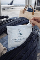Hand holding a LL Living laundry detergent pack over a suitcase with an airplane in the background